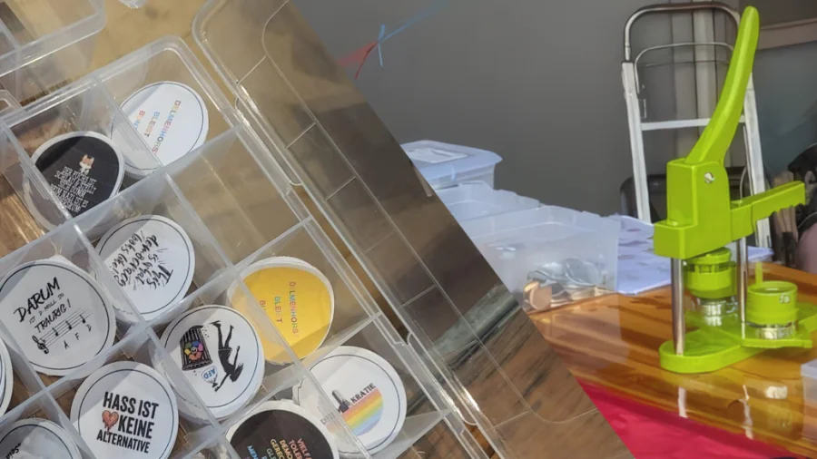 Nahaufnahme einer Button-Werkstatt: Eine leuchtend grüne Buttonpresse steht neben einer Box voller fertiger Button-Motive mit klaren Botschaften, wie "HASS IST KEINE ALTERNATIVE".